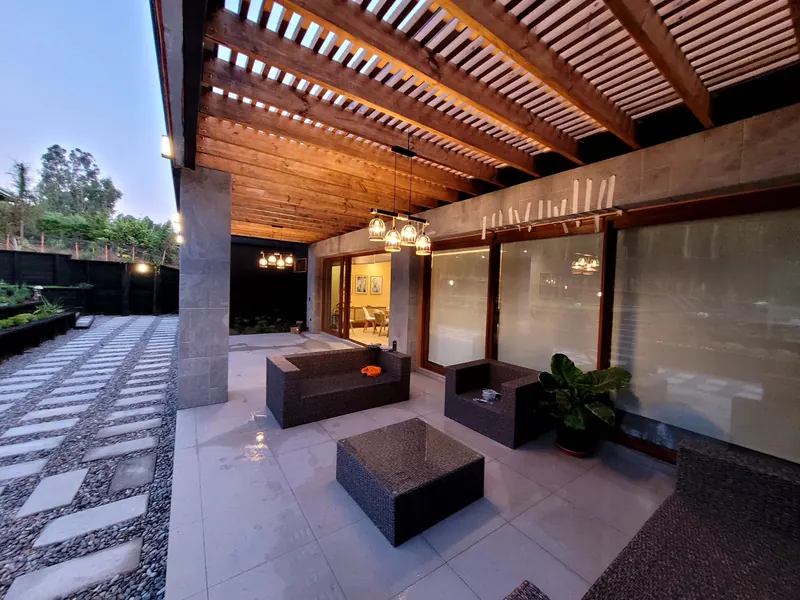 Terraza techada terminada con pergola de madera, lámparas colgantes y porcelanato